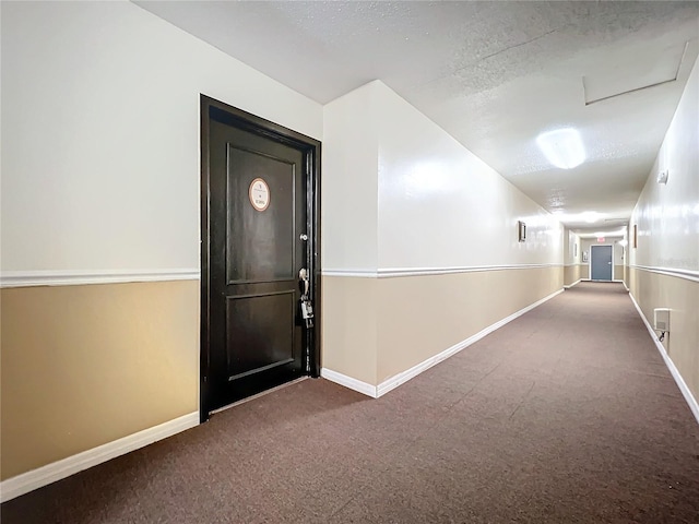 corridor with carpet, baseboards, and a textured ceiling