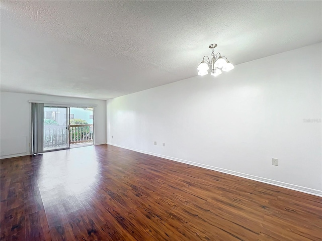 spare room featuring a chandelier, a textured ceiling, dark wood finished floors, and baseboards