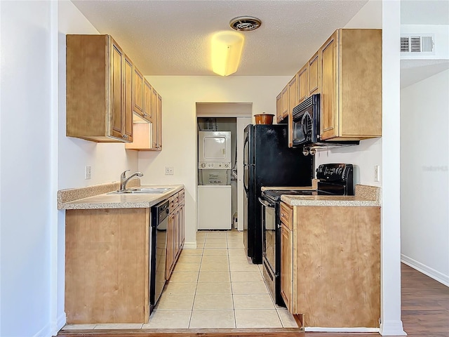 kitchen featuring stacked washer and dryer, visible vents, light countertops, black appliances, and a sink