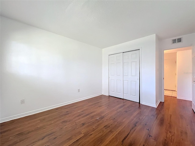 unfurnished bedroom with baseboards, visible vents, dark wood finished floors, and a closet