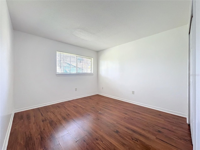 unfurnished room with baseboards, dark wood finished floors, and a textured ceiling