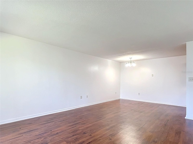 spare room with dark wood-style floors, a textured ceiling, baseboards, and a notable chandelier