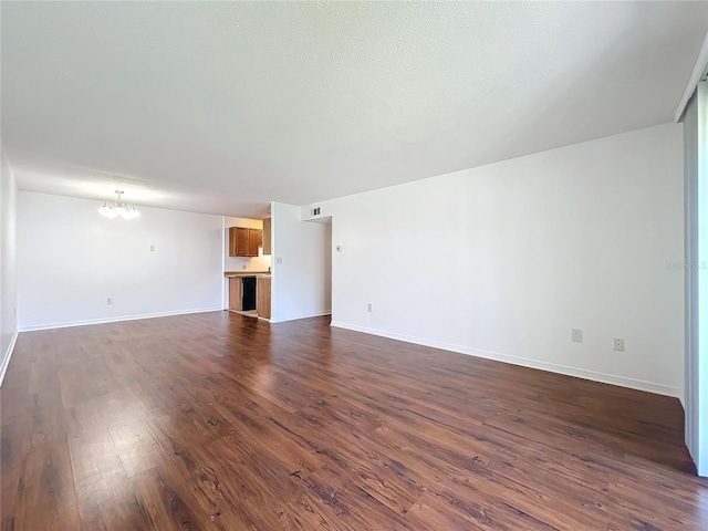 unfurnished living room featuring baseboards, dark wood finished floors, and a notable chandelier