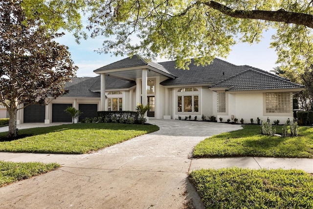 view of front of home featuring a tiled roof, a front lawn, an attached garage, and driveway