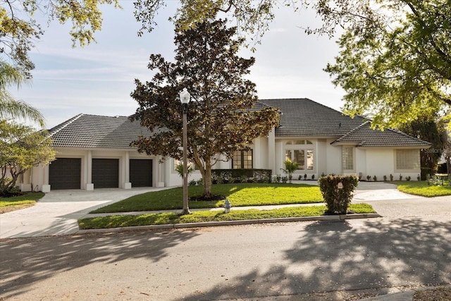 view of front facade featuring a garage, concrete driveway, a front lawn, and a tiled roof