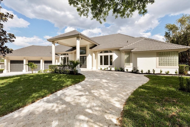 mediterranean / spanish home with stucco siding, a front yard, a garage, driveway, and a tiled roof