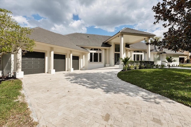 view of front of property with a garage, a tile roof, decorative driveway, a front yard, and stucco siding