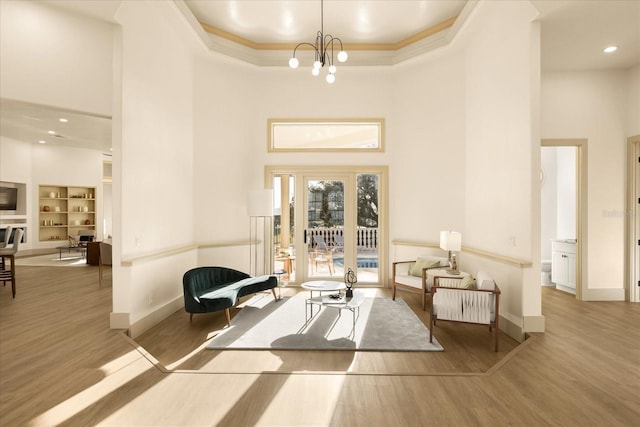 interior space with baseboards, a towering ceiling, ornamental molding, wood finished floors, and a chandelier