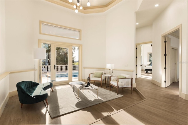 living area with a towering ceiling, an inviting chandelier, ornamental molding, wood finished floors, and baseboards