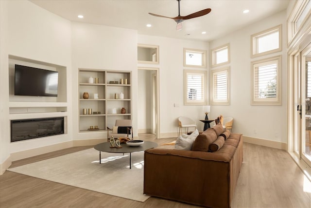 living room featuring baseboards, recessed lighting, a glass covered fireplace, and light wood-style floors