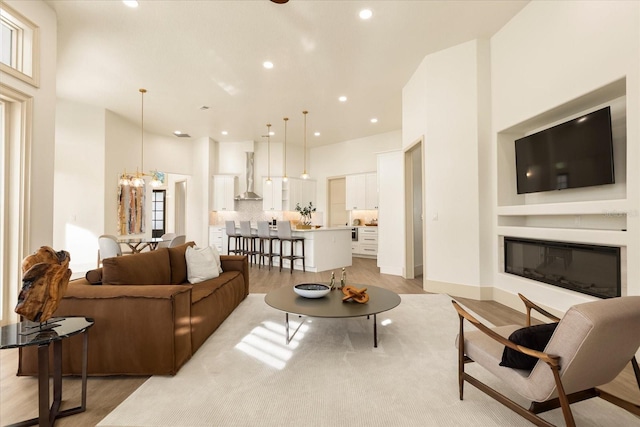 living room featuring recessed lighting, a glass covered fireplace, a chandelier, light wood-type flooring, and baseboards