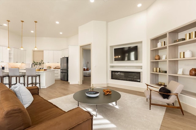 living area with a high ceiling, a glass covered fireplace, and light wood-style floors