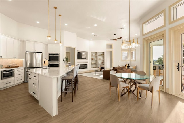 dining area featuring built in shelves, a fireplace, recessed lighting, a towering ceiling, and light wood-type flooring