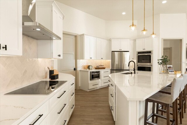 kitchen featuring appliances with stainless steel finishes, a kitchen breakfast bar, a sink, and wall chimney exhaust hood