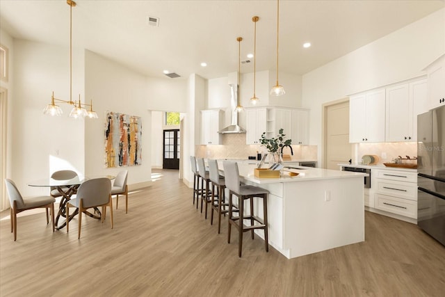 kitchen with wall chimney range hood, light wood-style flooring, a large island with sink, and freestanding refrigerator