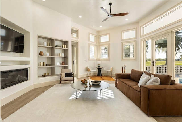 living area featuring recessed lighting, wood finished floors, a ceiling fan, built in features, and a glass covered fireplace