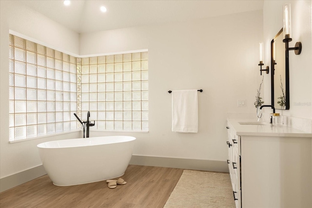 full bathroom with a freestanding tub, vanity, baseboards, and wood finished floors