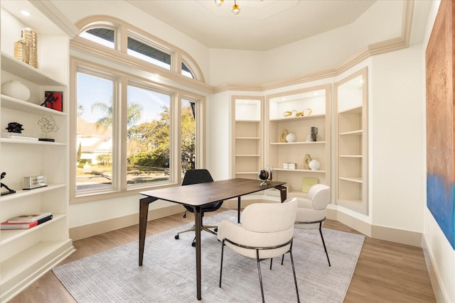 home office with light wood-style floors, built in shelves, and baseboards