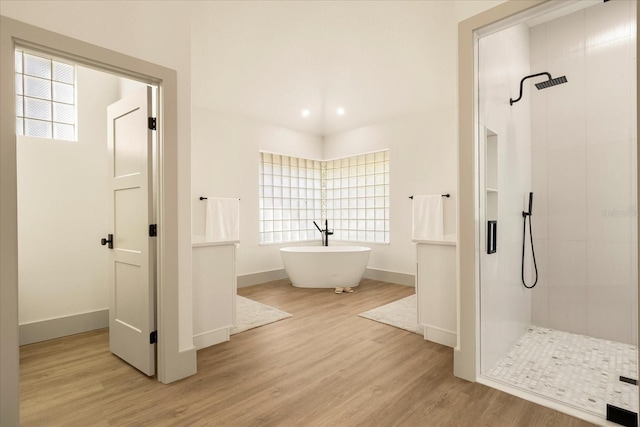 bathroom featuring baseboards, a tile shower, a freestanding bath, and wood finished floors