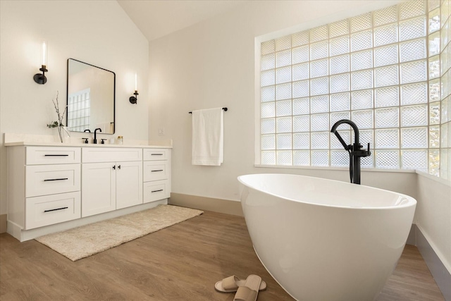 full bathroom with baseboards, a soaking tub, wood finished floors, vaulted ceiling, and vanity