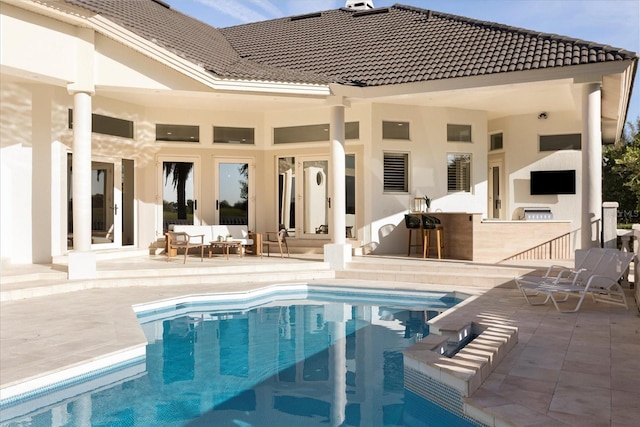 rear view of property featuring a patio area, an outdoor living space with a fireplace, an outdoor pool, and a tiled roof