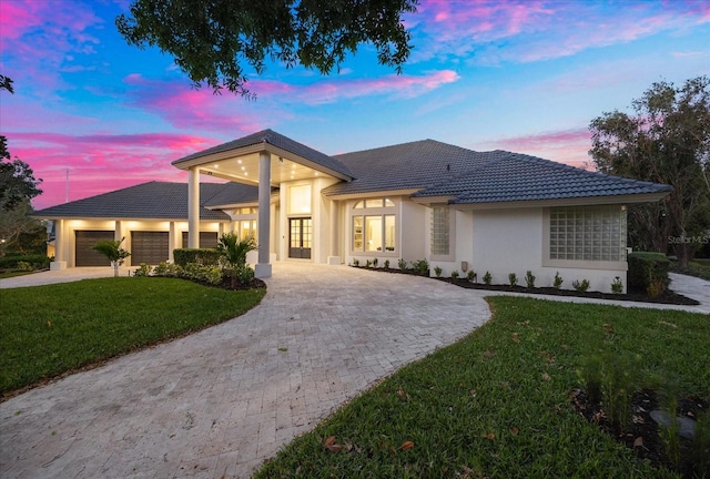 prairie-style home featuring an attached garage, stucco siding, a tile roof, decorative driveway, and a lawn