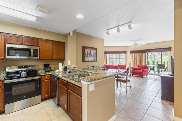 kitchen featuring light tile patterned floors, a textured ceiling, a peninsula, open floor plan, and appliances with stainless steel finishes