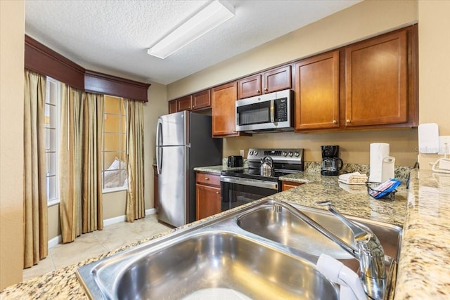 kitchen featuring baseboards, appliances with stainless steel finishes, a textured ceiling, a sink, and light tile patterned flooring