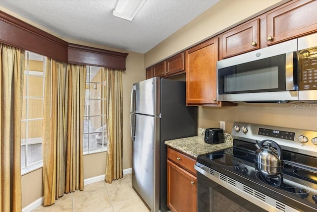 kitchen with baseboards, appliances with stainless steel finishes, light stone countertops, a textured ceiling, and light tile patterned flooring