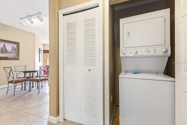 laundry room featuring light tile patterned floors, laundry area, baseboards, rail lighting, and stacked washing maching and dryer