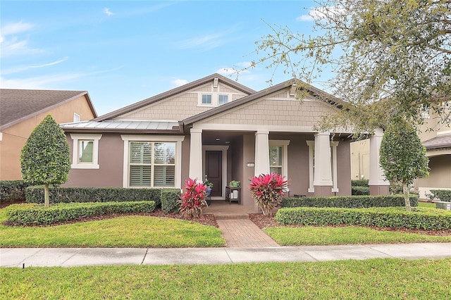 craftsman-style house featuring stucco siding, a front lawn, a standing seam roof, a porch, and metal roof