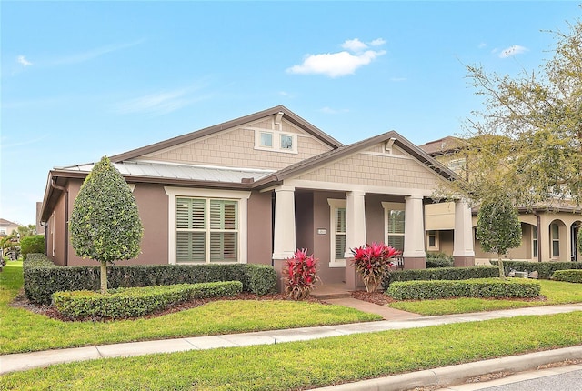 craftsman-style house featuring stucco siding, metal roof, and a front lawn