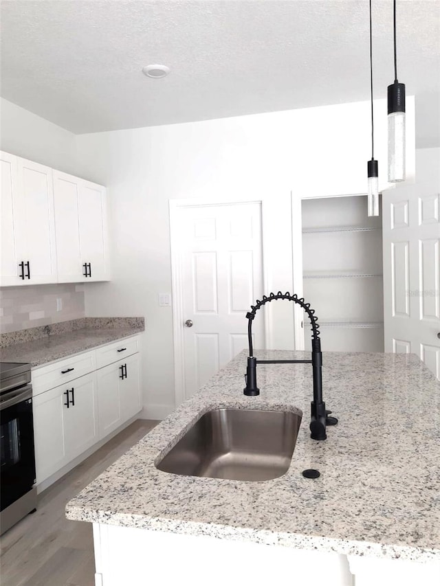 kitchen featuring a sink, light wood-style flooring, white cabinetry, hanging light fixtures, and stainless steel electric stove