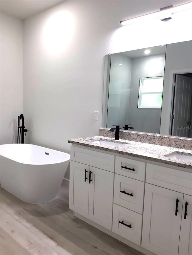 bathroom featuring double vanity, wood finished floors, a freestanding bath, and a sink