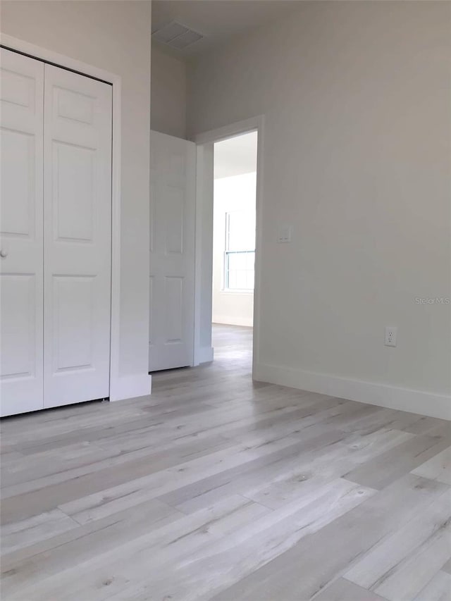 unfurnished bedroom featuring light wood-type flooring, a closet, visible vents, and baseboards