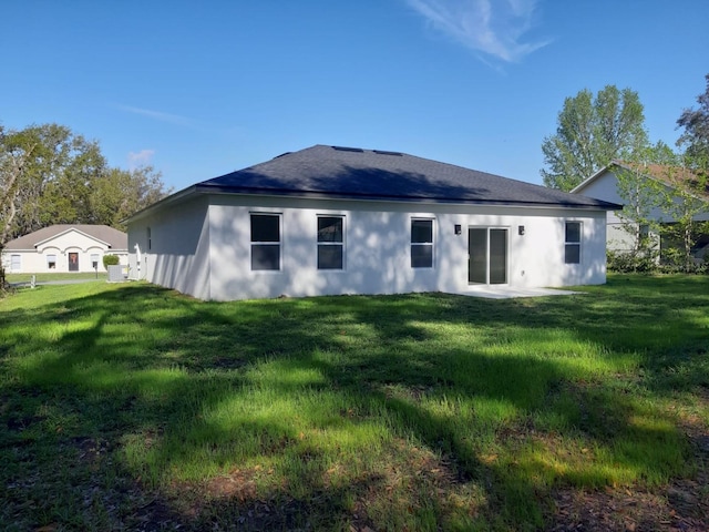 rear view of house with a lawn, roof with shingles, and stucco siding