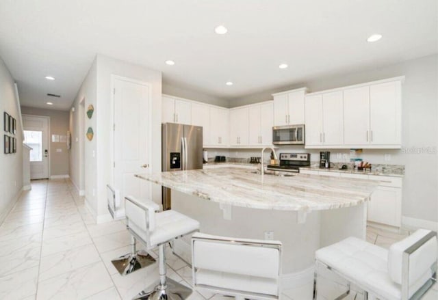 kitchen with light stone counters, a kitchen island with sink, a kitchen breakfast bar, white cabinets, and appliances with stainless steel finishes