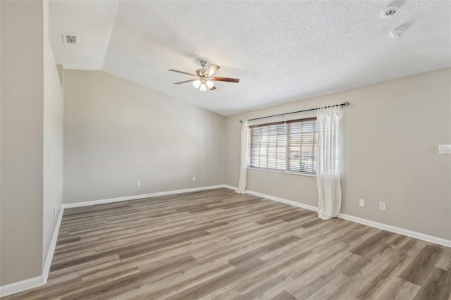 empty room with wood finished floors, visible vents, ceiling fan, vaulted ceiling, and a textured ceiling