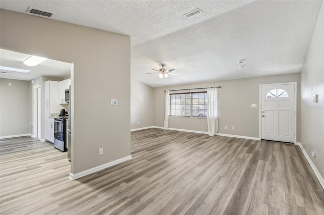 unfurnished living room with visible vents, baseboards, light wood-style floors, and a textured ceiling