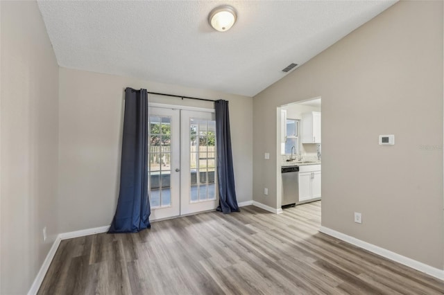 unfurnished room with visible vents, light wood-type flooring, a sink, french doors, and lofted ceiling