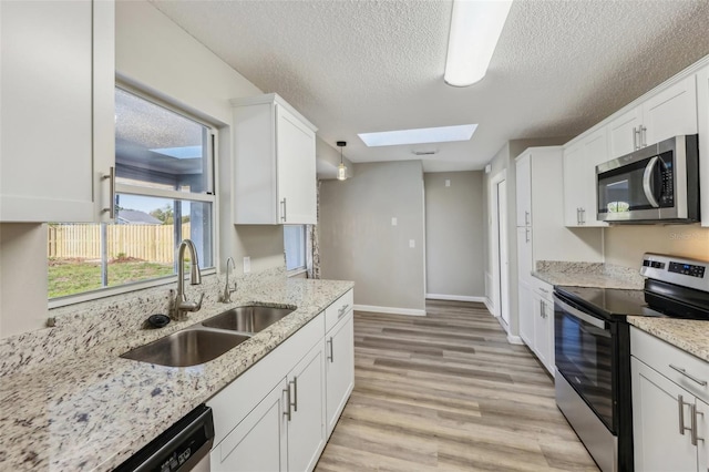 kitchen with a skylight, a sink, appliances with stainless steel finishes, white cabinetry, and light wood-type flooring