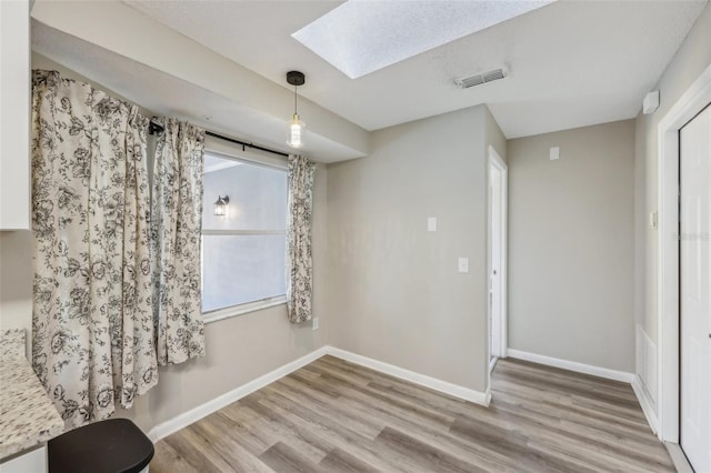 unfurnished room featuring wood finished floors, visible vents, baseboards, and a skylight