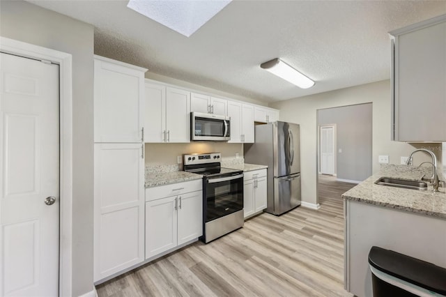 kitchen with light stone counters, light wood finished floors, a skylight, a sink, and appliances with stainless steel finishes