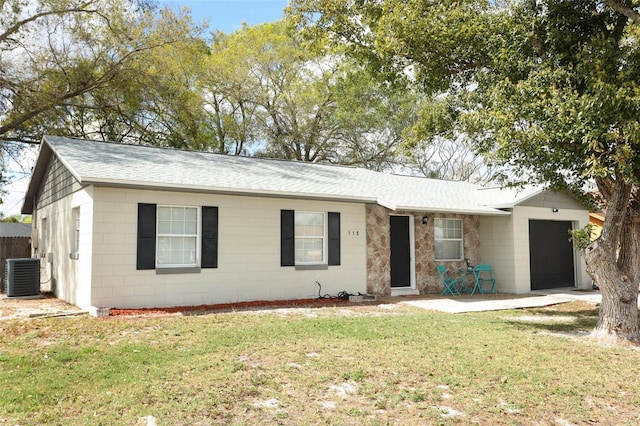 ranch-style home with a shingled roof, concrete block siding, an attached garage, cooling unit, and a front yard