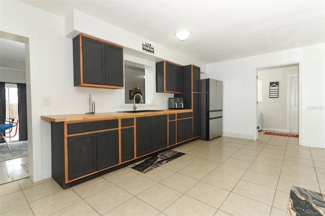 kitchen featuring light tile patterned floors, a textured ceiling, a sink, wood counters, and freestanding refrigerator