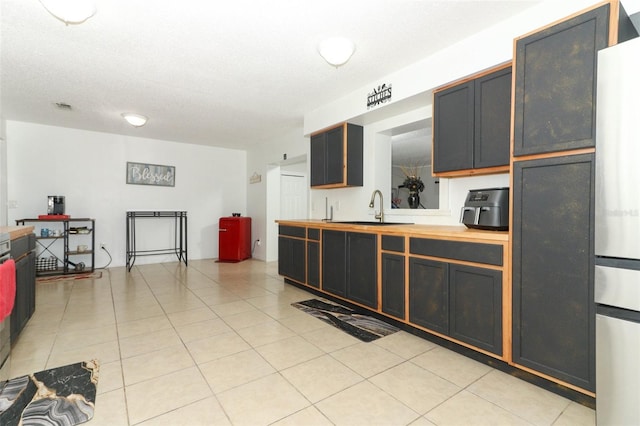 kitchen with light tile patterned floors, a sink, visible vents, wooden counters, and freestanding refrigerator