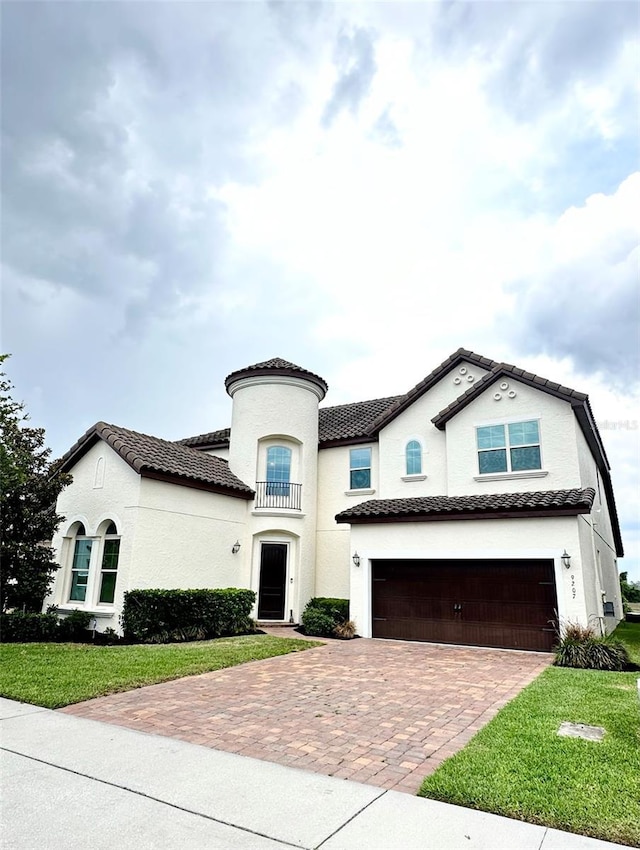 view of front of house featuring a front yard, stucco siding, a garage, a tiled roof, and decorative driveway