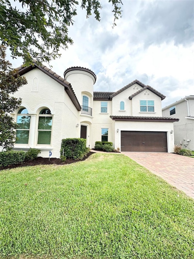 mediterranean / spanish house with an attached garage, stucco siding, a front lawn, a tile roof, and decorative driveway