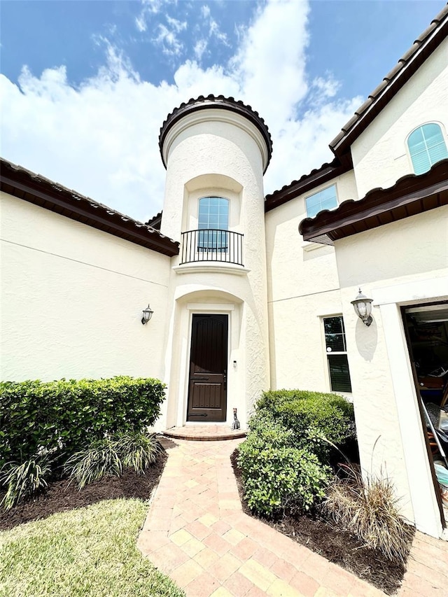 entrance to property featuring stucco siding, a balcony, and a tiled roof