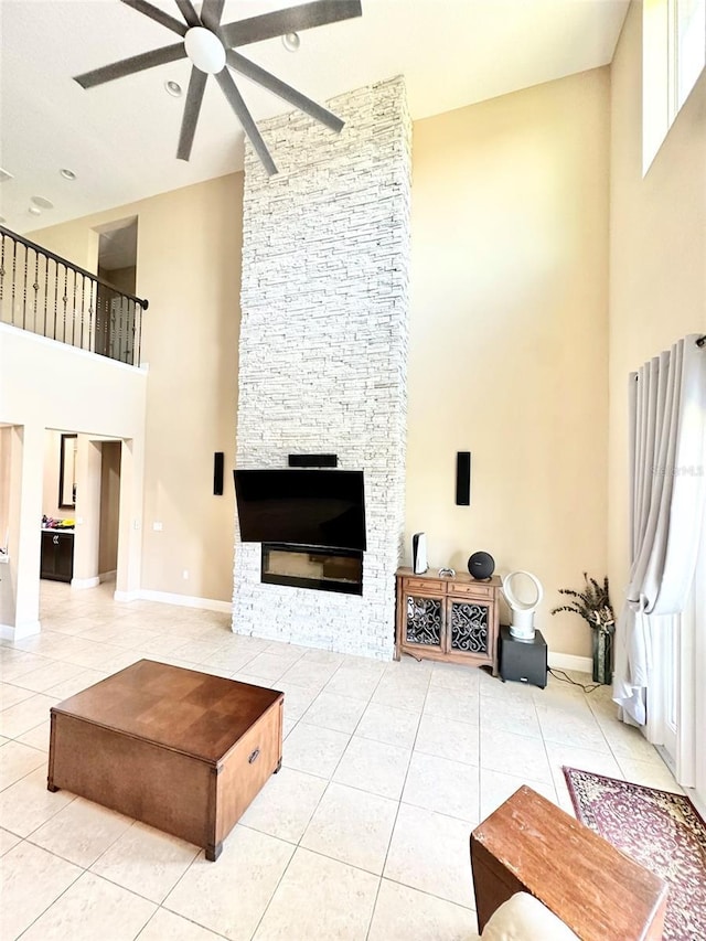 living area featuring a stone fireplace, light tile patterned flooring, baseboards, and ceiling fan